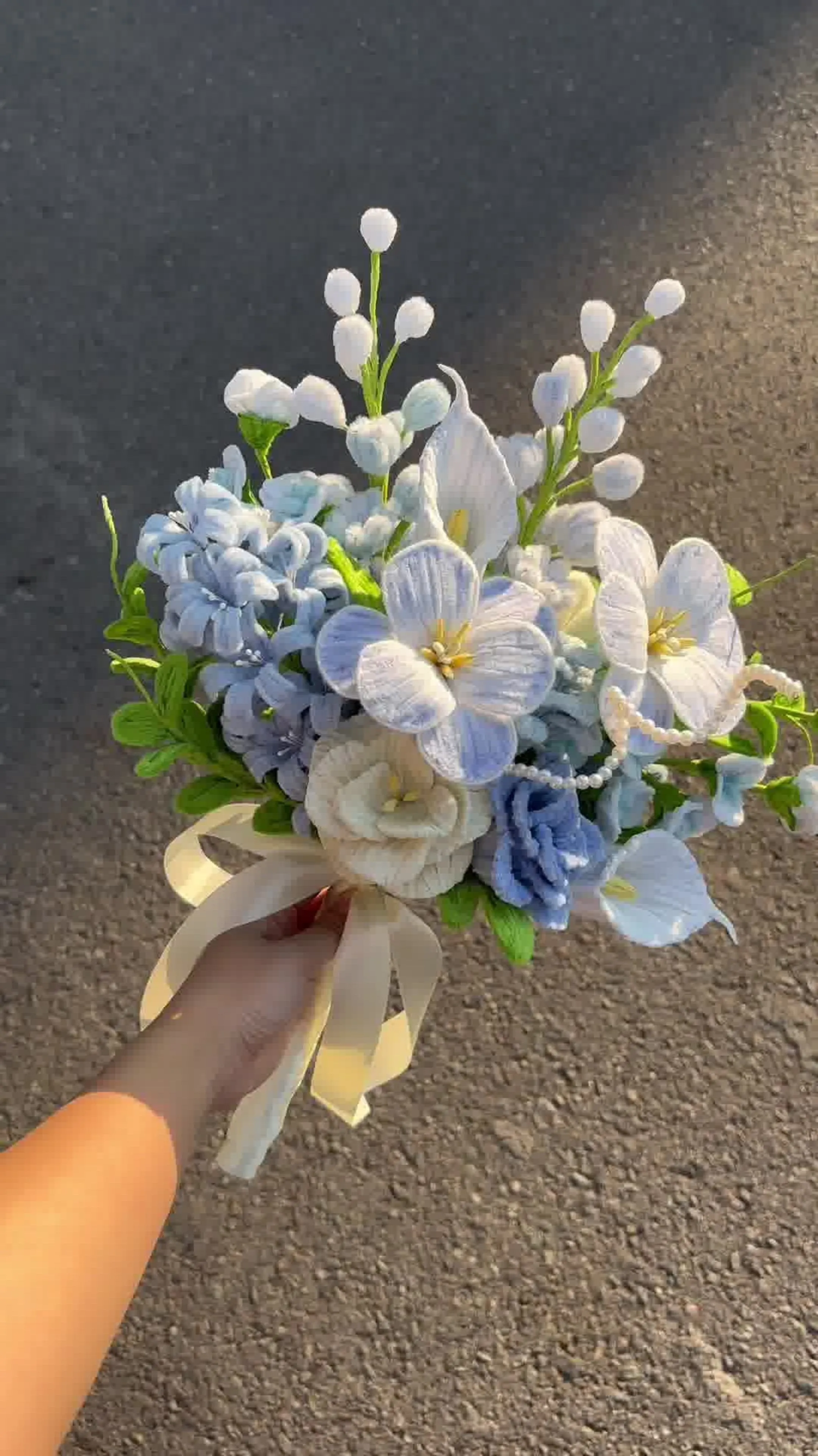 Ramo de flores blancas y celestes sostenido al aire libre